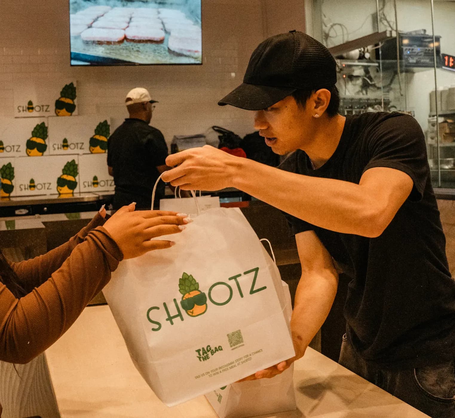 A crew member handing a Shootz takeout bag across the counter to a guest