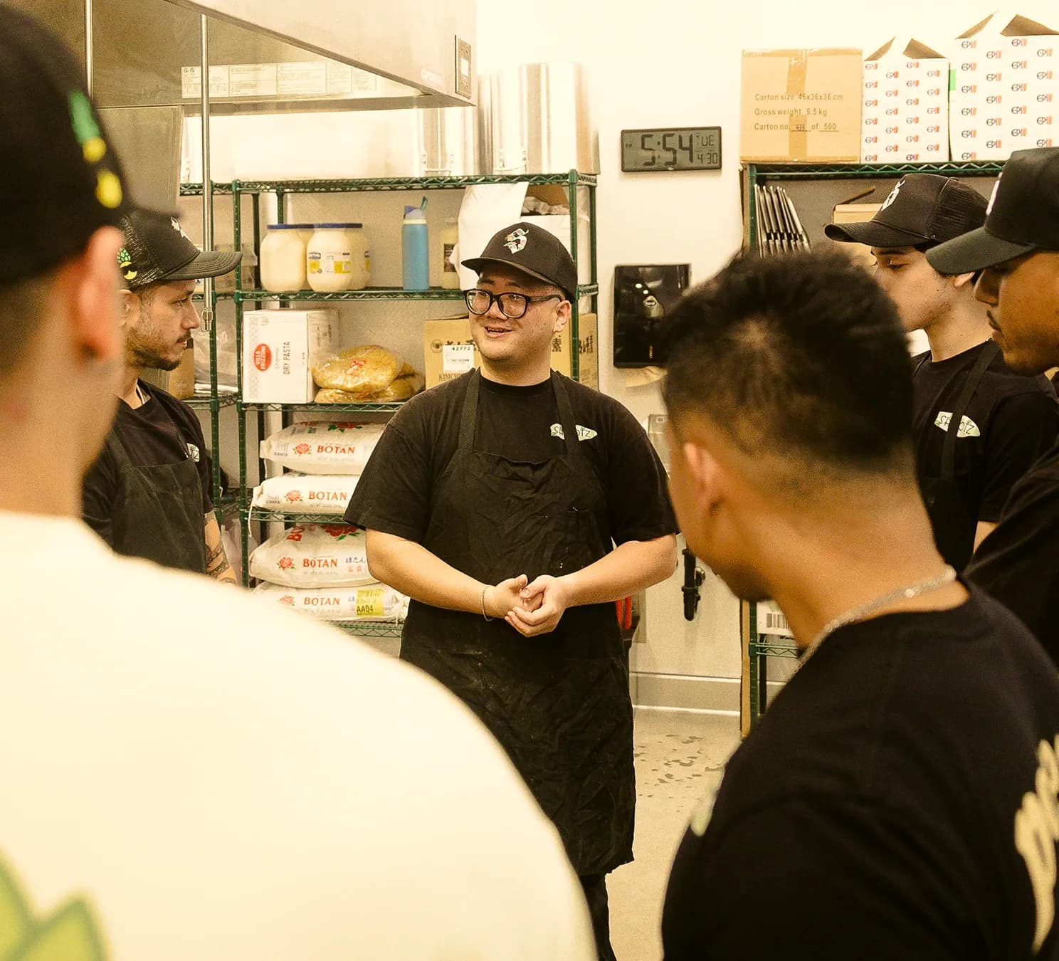 A shift lead smiling while leading a pre-shift huddle with the kitchen crew