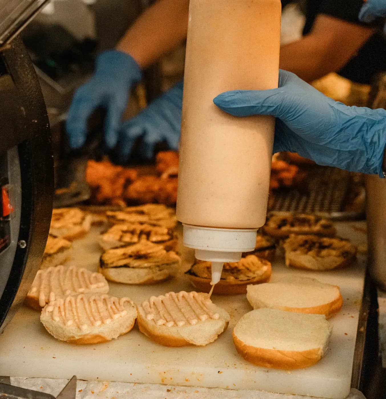 Gloved hands saucing a row of toasted sando buns